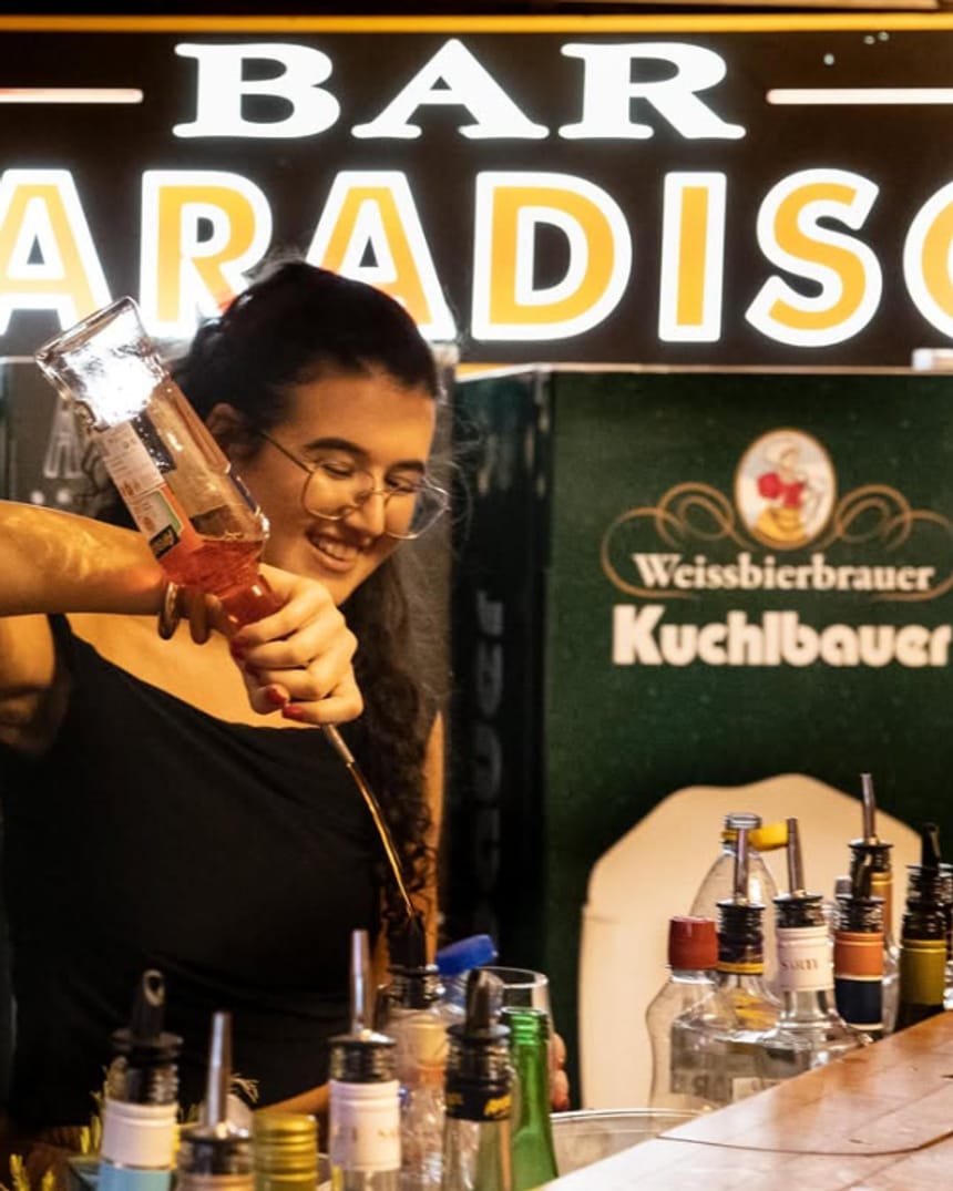 Junge Frau schenkt an der Bar Paradiso ein, im Hintergrund der beleuchtete Schriftzug